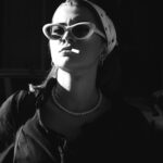 A stylish woman wearing sunglasses and pearls in a dramatic black and white portrait.